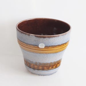 May include: A brown and blue ceramic planter with a striped design. The planter has a wide opening and a rounded bottom.