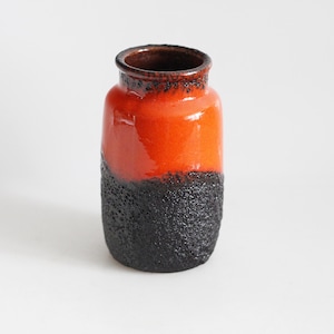 Puede incluir: Un jarrón de cerámica con una mitad superior naranja brillante y una mitad inferior negra texturizada. El jarrón tiene forma cilíndrica con un borde ligeramente ensanchado y un interior marrón oscuro. Es un objeto decorativo.