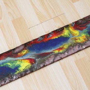 May include: A long, rectangular piece of art with a colorful abstract design. The design features swirls of blue, red, yellow, and green paint.