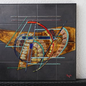 Peut inclure: Une œuvre d'art murale en céramique noire et brune avec des formes géométriques abstraites et des lignes dans des tons de bleu, vert, rouge et jaune. La pièce est signée "KM" dans le coin inférieur droit.