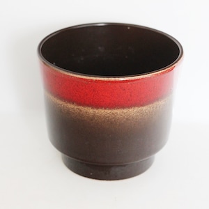 Op de afbeelding: Een bruine keramische plantenpot met een rode band rond het midden. De pot heeft een licht uitlopende bovenkant en een afgeronde bodem.