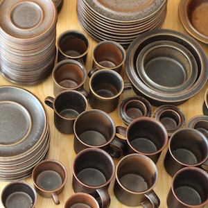 Peut inclure: Une collection de tasses et d'assiettes en céramique brune. Les tasses ont une forme arrondie et une finition lisse. Les assiettes sont rondes et ont un bord légèrement surélevé.