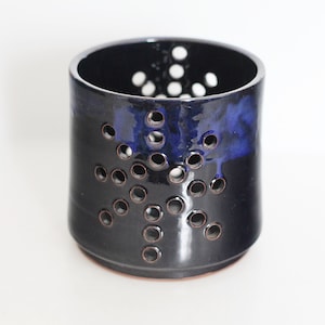 Op de afbeelding: Een donkerblauwe keramische bestekhouder met een sneeuwvlokkenontwerp en gaten voor drainage.