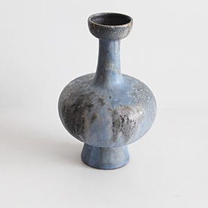 Puede incluir: Un jarrón de cerámica con un cuerpo bulboso y un cuello estrecho. El jarrón es principalmente azul con detalles grises y plateados moteados. La abertura es de color gris oscuro. El jarrón tiene una base de pedestal.