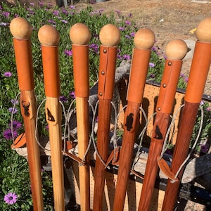 May include: Seven wooden walking sticks with leather straps and decorative carvings. The sticks are different colors and have different designs.