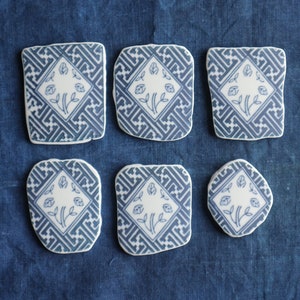 May include: Six blue and white ceramic coasters with a geometric pattern and a floral design. The coasters are arranged in two rows of three.
