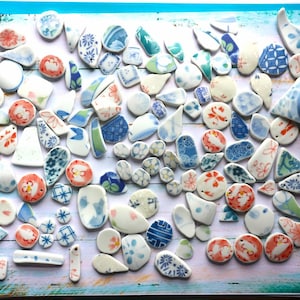 May include: A collection of numerous small, irregular ceramic shards featuring a variety of patterns, including floral motifs, geometric grids, and abstract designs in shades of blue, orange, red, green, and white, scattered across a surface.