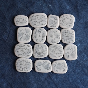 Puede incluir: Un conjunto de 15 azulejos de cerámica blanca con un diseño floral en blanco y negro. Los azulejos están dispuestos en forma de cuadrado.