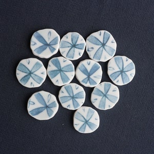 May include: Ten white ceramic tiles with a blue floral design. Each tile features a stylized flower with four petals.