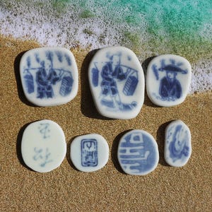 May include: Seven blue and white ceramic tiles with various designs. The tiles feature images of people, flowers, and abstract patterns.