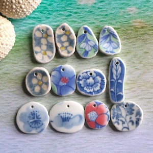 May include: A collection of ceramic pendants with floral designs in blue, white, and red. The pendants vary in shape and size, featuring patterns like flowers and leaves. Each pendant has a small hole for stringing.