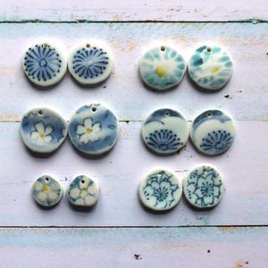 Puede incluir: Una colección de diez colgantes de cerámica redondos dispuestos en parejas, con varios patrones florales en azul y blanco, incluyendo crisantemos y flores de cerezo, cada uno con un pequeño orificio en la parte superior.