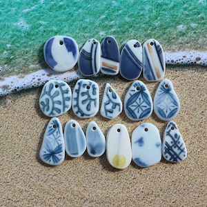 May include: A collection of 15 ceramic pendants with blue and white designs. The pendants are shaped like teardrops and have a hole at the top for hanging. Some of the pendants have a yellow accent.