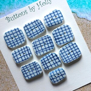 Könnte beinhalten: Eine Sammlung quadratischer, weißer Knöpfe mit blauem Gittermuster. Jeder Knopf hat zwei Löcher zum Annähen. Die Knöpfe sind auf einer weißen Karte mit dem Text "Buttons by Holly" in grüner Schrift angeordnet.