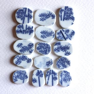 Puede incluir: Un conjunto de 15 azulejos de cerámica blanca con diseños de bambú azul. Los azulejos son de forma ovalada y tienen un acabado brillante.