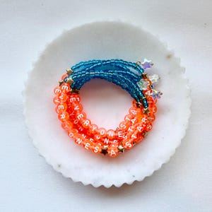 May include: A multi-strand beaded bracelet featuring translucent orange beads with white letter beads spelling EVERYONE IS A STAR, interspersed with small gold-tone star charms, and a section of translucent blue beads with iridescent star charms.