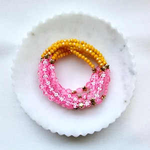 May include: A multi-strand beaded bracelet featuring yellow faceted beads and translucent pink round beads with white lettered text that reads EVERYONES A STAR, accented with small gold-toned star-shaped charms throughout the design.