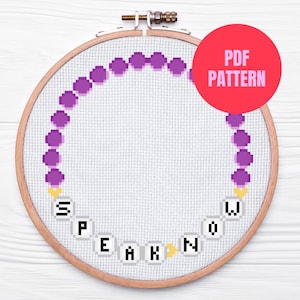 Op de afbeelding: Een kruissteekpatroon in een houten borduurring. Het ontwerp toont een cirkel van paarse gepixelde kralen en de woorden "SPEAK NOW" in gepixelde letters. Een rode cirkel met "PDF PATTERN" staat rechtsboven.