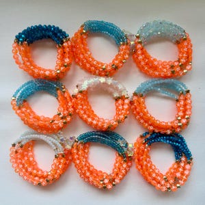 May include: Nine circular bracelets arranged in a grid, each featuring orange letter beads spelling EVERYONES STAR interspersed with small gold star beads. The top half of each bracelet consists of various coloured faceted beads.