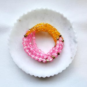 May include: A stack of three beaded bracelets featuring translucent pink beads with white letter beads spelling out EVERYONES STAR, interspersed with small gold-toned star-shaped charms, and a top layer of faceted yellow beads.