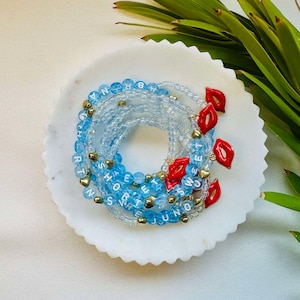May include: A set of blue beaded bracelets with white letter beads spelling out words like "Sweet" and "June". Each bracelet has a red lip charm.