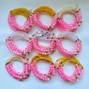 May include: Nine circular bracelets arranged in a grid, each featuring pink letter beads spelling EVERYONES STAR interspersed with small gold-toned star charms. The bracelets incorporate various bead colours including yellow, white, and iridescent clear.
