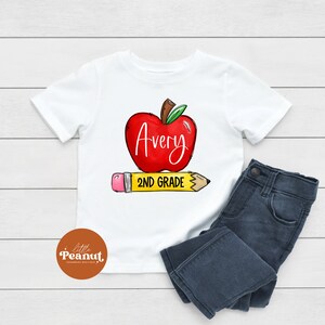 May include: White t-shirt with a red apple graphic and the text "Avery 2ND GRADE" on a yellow pencil.