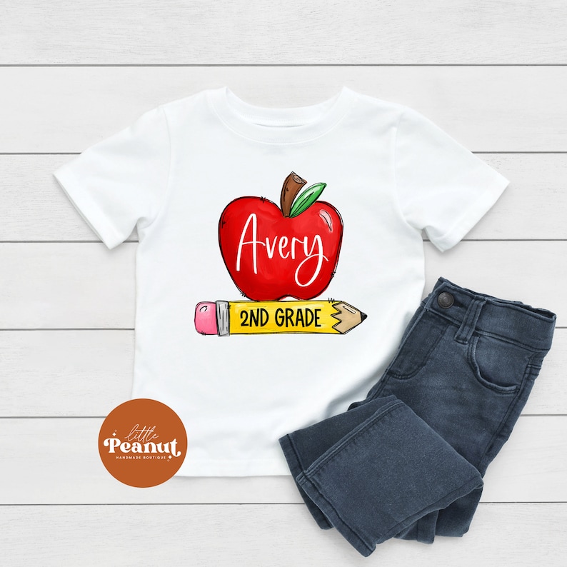 May include: White t-shirt with a red apple graphic and the text "Avery 2ND GRADE" on a yellow pencil.