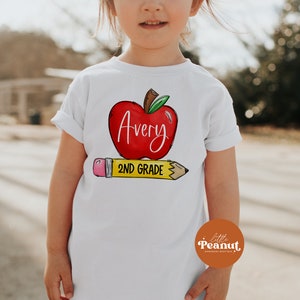 May include: White t-shirt with a red apple graphic and the text "Avery 2nd Grade" on a yellow pencil.