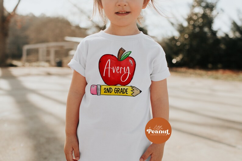 May include: White t-shirt with a red apple graphic and the text "Avery 2nd Grade" on a yellow pencil.