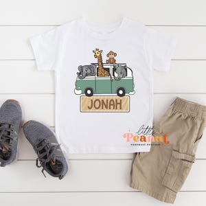 May include: White t-shirt with a green and white van with a giraffe, monkey, elephant, and rhino. The van has the name "Jonah" on the side.