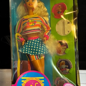 May include: Special Edition Barbie doll in original packaging. The doll wears a striped top, polka dot skirt, and has blonde hair. The packaging is pink and green with the words "Fun Barbie" and "POG" printed on it.