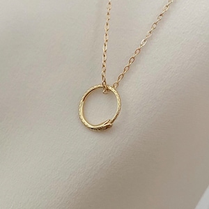Könnte beinhalten: Eine goldene Schlangenkettenkette mit einem goldenen Schlangenkreis-Anhänger.