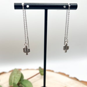 May include: A pair of silver chain earrings with a small cactus charm hanging from each chain.