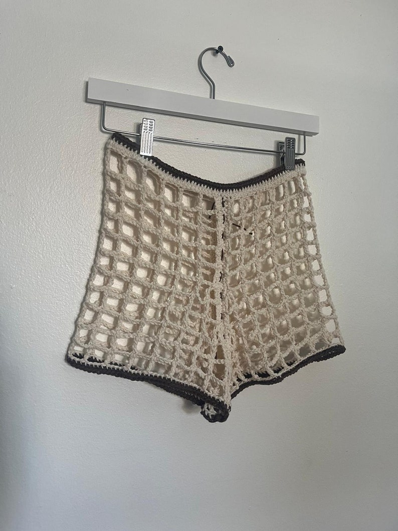 May include: White crochet shorts with a brown crocheted trim. The shorts are made of a lightweight, airy material and have a loose fit.