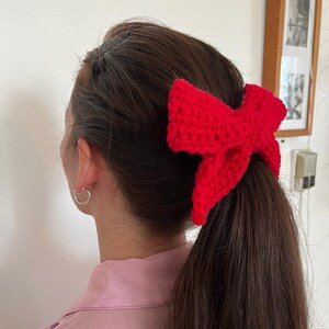 May include: A red crocheted bow hair tie worn in a ponytail.