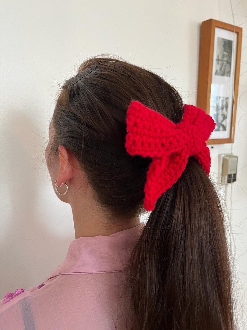 May include: A red crocheted bow hair tie worn in a ponytail.