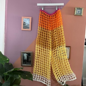 May include: Crocheted pants with a wide leg, featuring a multi-colored design. The pants are made of a lightweight, airy material and have a relaxed fit. The colors are pink, orange, yellow, and white.