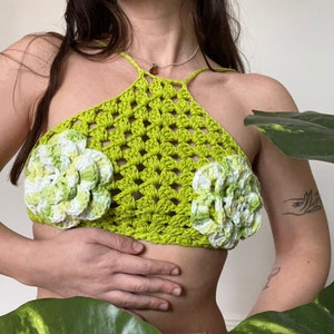 Op de afbeelding: Een limoengroen gehaakt haltertop met witte gehaakte bloemen op de borst.