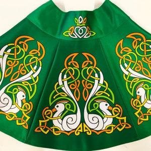 May include: Green Irish dance skirt with a white, orange, and green Celtic knot design featuring swans. The skirt has a green waistband with a white Celtic knot design.