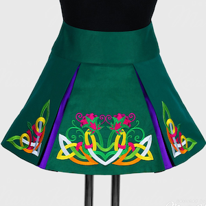 May include: A green dance skirt with a pleated design and a wide waistband. The skirt features colorful embroidered Celtic knot and floral patterns in pink, yellow, orange, and white. Purple fabric accents the sides.