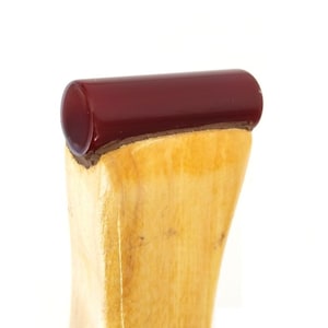 May include: Close-up of a wooden object with a dark red, cylindrical top. The wood has a light, natural color with visible grain. The top appears to be made of a glossy, smooth material.