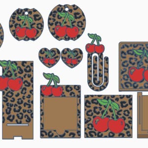 Puede incluir: Una colección de varios artículos decorativos con un diseño de cereza. Los artículos incluyen etiquetas redondas y en forma de corazón, un clip, un soporte para teléfono y un posavasos cuadrado. El fondo tiene un estampado de leopardo.