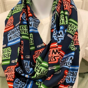 May include: A navy blue infinity scarf with a repeating pattern of the words "Star Wars" in red, blue, and green. The words are outlined in white and have a light saber graphic next to them.