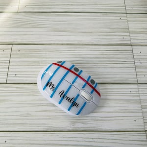 May include: A white computer mouse with a blue and white striped design and the text "Ms. Avalyn" written in black.