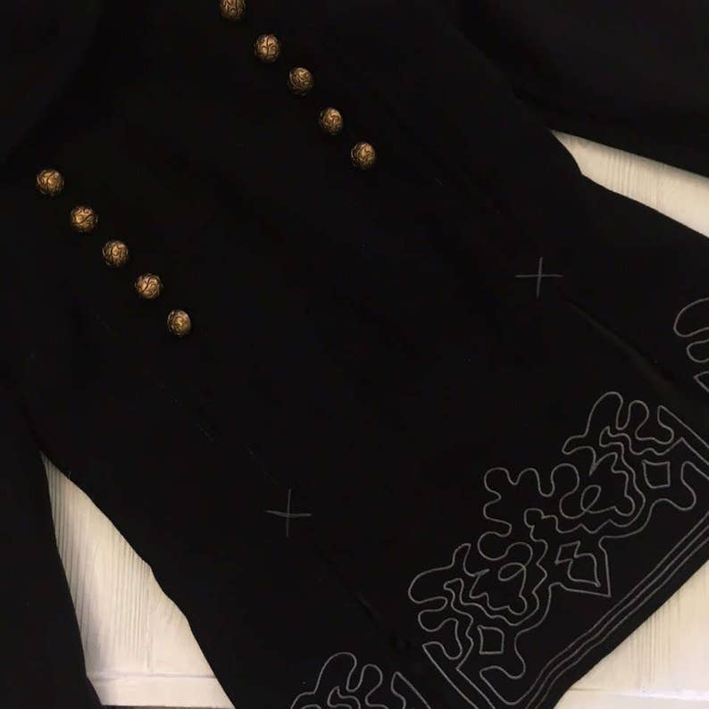 May include: A black jacket with gold buttons and a decorative embroidered design on the bottom.