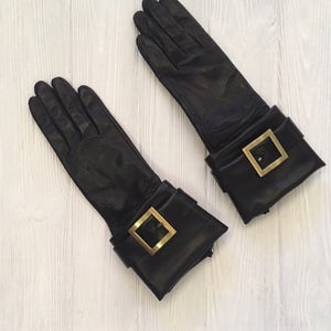 May include: A pair of black leather gloves with gold buckles on the cuffs.