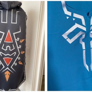 May include: A black hooded cape with a white and orange geometric design. The cape has a white and silver design on the front.