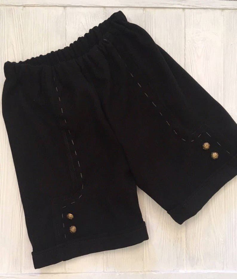 May include: Black shorts with a cuffed hem and decorative stitching. The shorts have three gold buttons on each side.