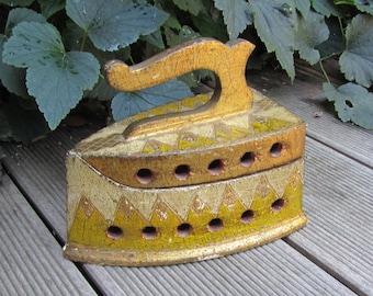 May include: A vintage wooden iron painted in gold and yellow with a decorative pattern. The iron has a handle and multiple holes on the top.